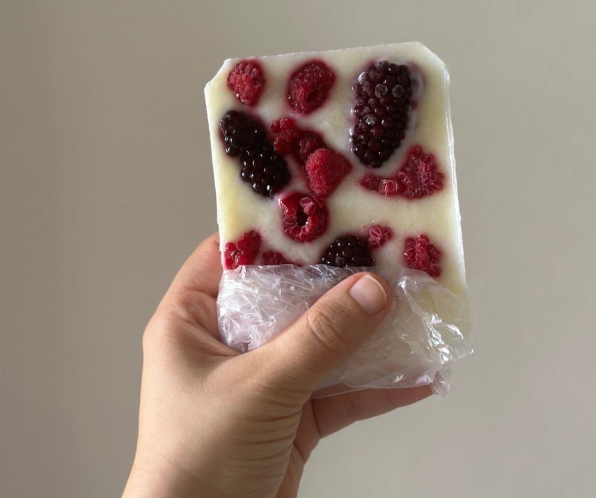 Una mano sosteniendo una barrita de helado casero de yogur con frutos rojos frescos.